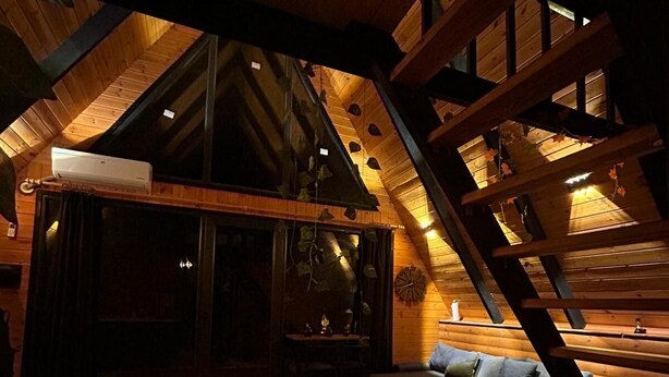 A cozy, log cabin-style room with a high ceiling, a red patterned rug, a sofa, and a staircase. - MİRA BUNGALOV (Trabzon)