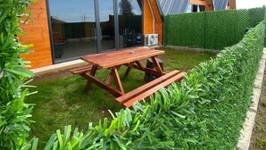 A modern A-frame house with a large glass door, a wooden deck, and a well-maintained lawn. - MİRA BUNGALOV (Trabzon)