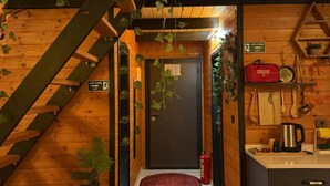 A wooden interior with a staircase, a red carpet, a door labeled "ACIL CIKIS EXIT", and a kitchen area with a kettle and utensils. - MİRA BUNGALOV (Trabzon)