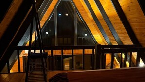 A high-ceilinged attic bedroom with a wooden sloped roof, a ladder leading to a lofted area, and a large window providing a view of the interior. - MİRA BUNGALOV (Trabzon)