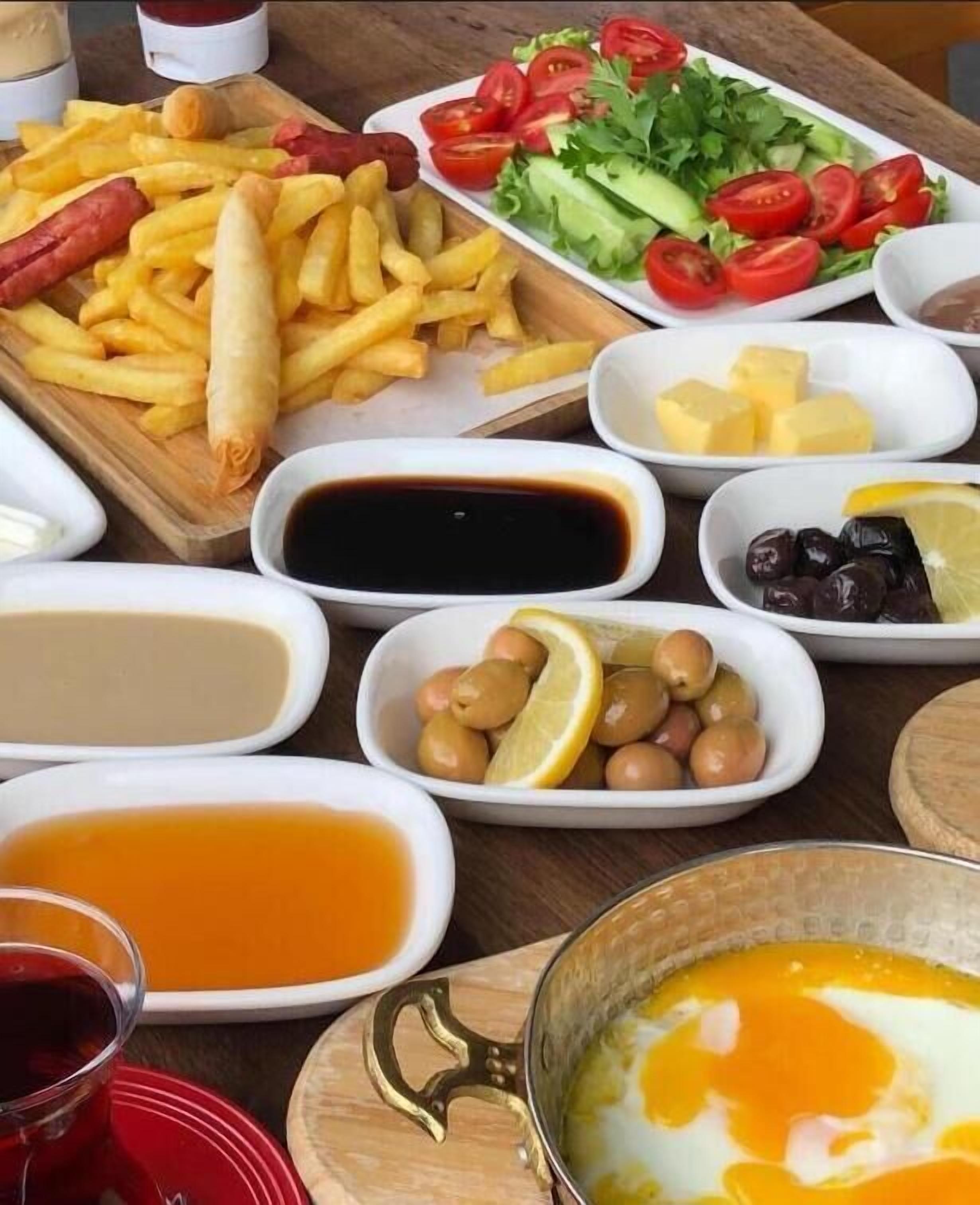 Una mesa con varios platos, entre ellos papas fritas, ensalada, aceitunas y un cuenco de huevos.