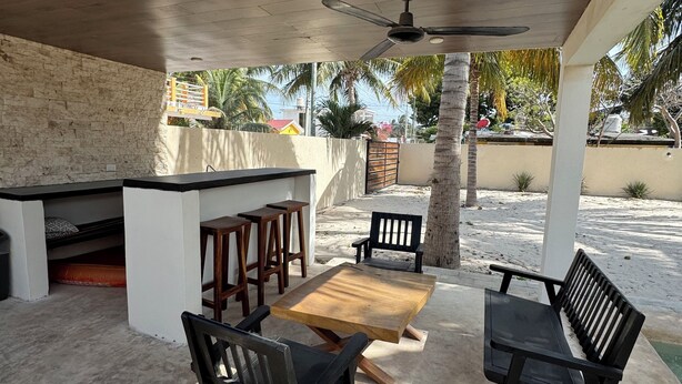 Une terrasse extérieure avec une table et des chaises en bois, un ventilateur de plafond et un mur en pierre.