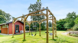 En gungställning i trä på en gräsig gård, med en röd byggnad i bakgrunden.