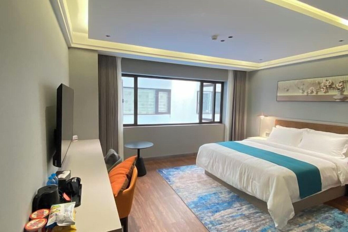 A hotel room with a bed, a desk, a chair, a television, and a window with a view.