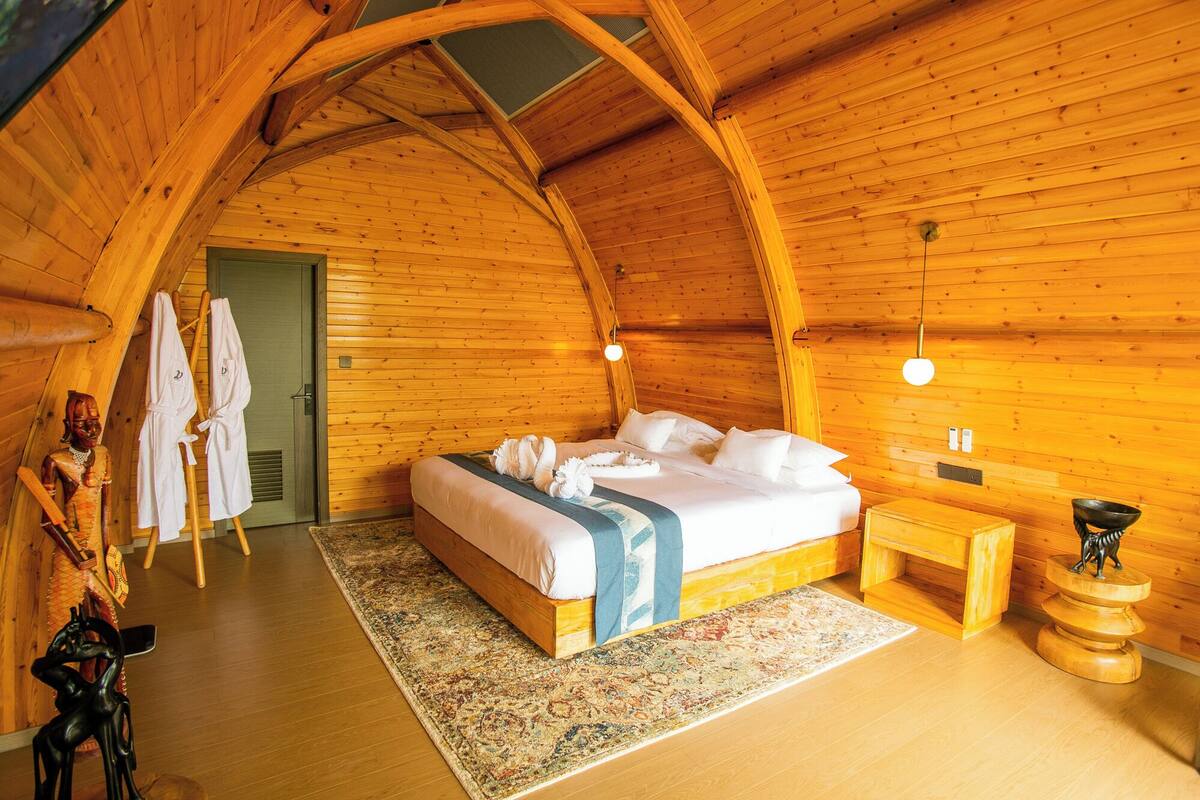 A cozy, wooden cabin room with a bed, bedside table, and a small wooden stool.