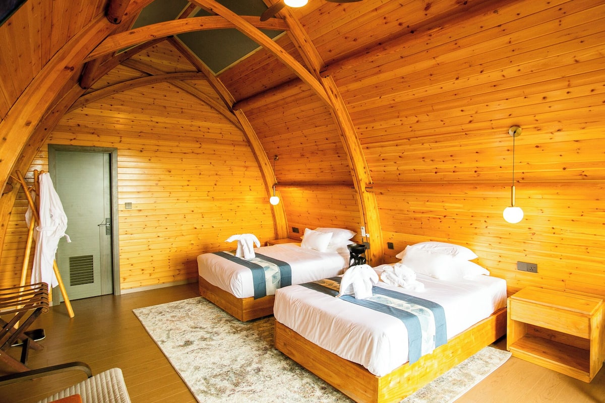 A cozy cabin room with two beds, wooden walls, and a sloped ceiling.