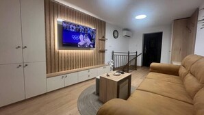 Olohuoneessa on seinälle asennettu televisio, jonka takana on puupanelointi, ruskea sohva ja pieni sohvapöytä.