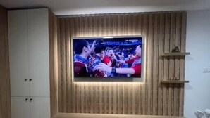 Olohuone, jossa on seinälle kiinnitetty televisio, pieni pöytä, jossa on kulho täynnä naposteltavaa, ja kaukosäädin.