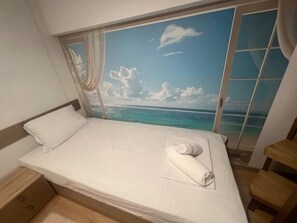 A bed with a view of the ocean through a window, a wooden nightstand, and a wooden chair. - Angel Home 2bdrm Modern Apartment (Varna)