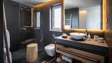 Une salle de bain moderne avec une douche à parois de verre, un tabouret en bois, des toilettes blanches et un meuble-lavabo doté d’un grand miroir.