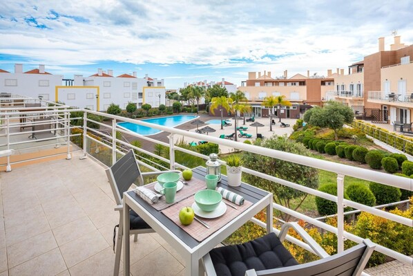 Un balcon avec une table dressée pour deux personnes, donnant sur une piscine et un jardin.