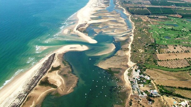 Eine Luftaufnahme einer Küstenregion mit Strand, Fluss und landwirtschaftlichen Feldern.