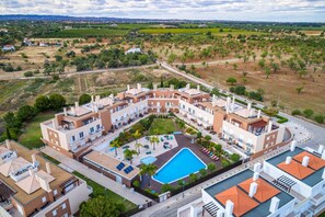 Un hotel moderno con piscina, varios balcones y un patio ajardinado.