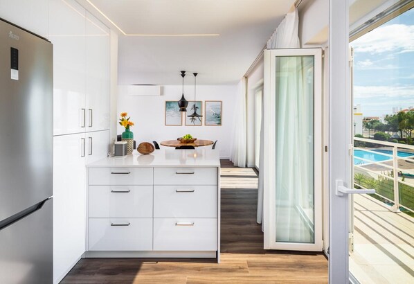 Una cocina moderna con una isla central, armarios blancos y vistas a una piscina.