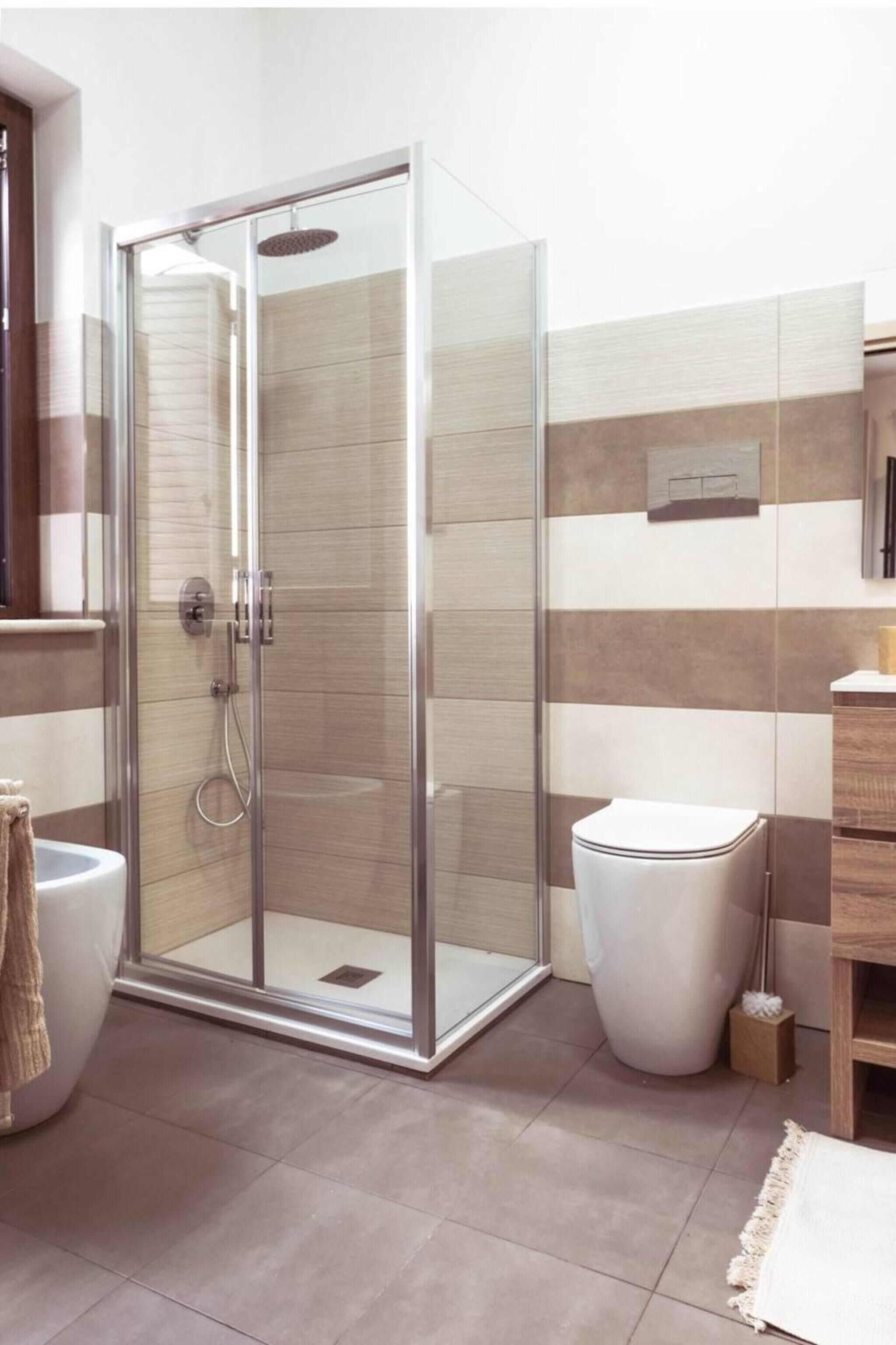A modern bathroom with a glass-enclosed shower, a white toilet, and a wooden vanity.