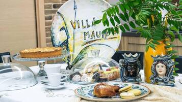 Una mesa dispuesta con diversos pasteles y un pastel, un plato decorativo con el texto 'VILLA MAURO' y un jarrón amarillo con diseño de rostro.