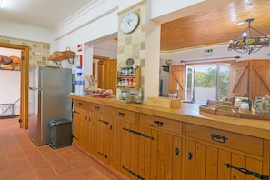 A kitchen with wooden cabinets, a stainless steel refrigerator, a clock, and a chandelier.
