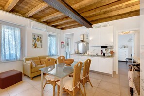 Una cucina moderna con mobili bianchi, una cappa in acciaio inossidabile e una zona pranzo con tavolo in vetro e sedie in vimini.