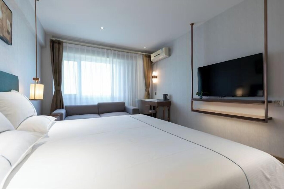 A hotel room with a large bed, a TV mounted on the wall, a small table, and a sofa.