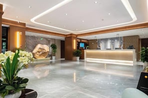 A modern hotel lobby with a reception desk, seating area, and decorative plants.