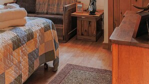 Een gezellige kamer met een houten plafondventilator, een raam met uitzicht, een houten garderobe, een tafeltje met een lamp, een bank en een bed met sprei.