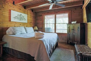 Quarto de cabana de madeira com cama, ventilador de teto, janela e armário.