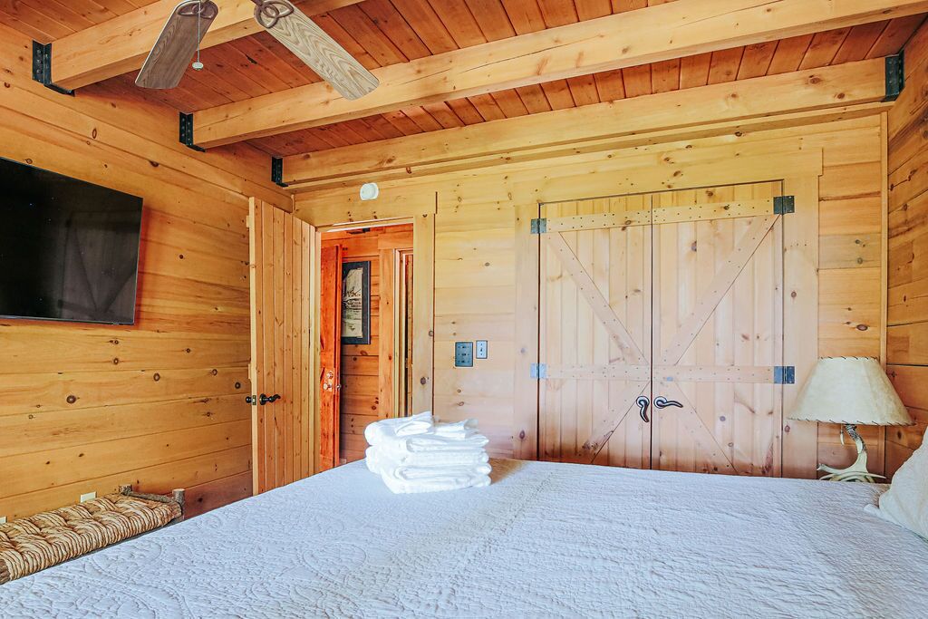 Ein Schlafzimmer in einer Holzhütte mit einem Bett, einem Stapel Handtücher, einer Lampe und einer Holztür.