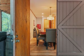 Eine Holztür führt in einen Essbereich mit einer Chandelüster, Stühlen und einem Tisch.