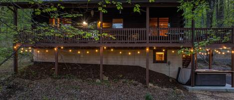 Una cabaña con terraza de madera, luces colgantes y un porche.