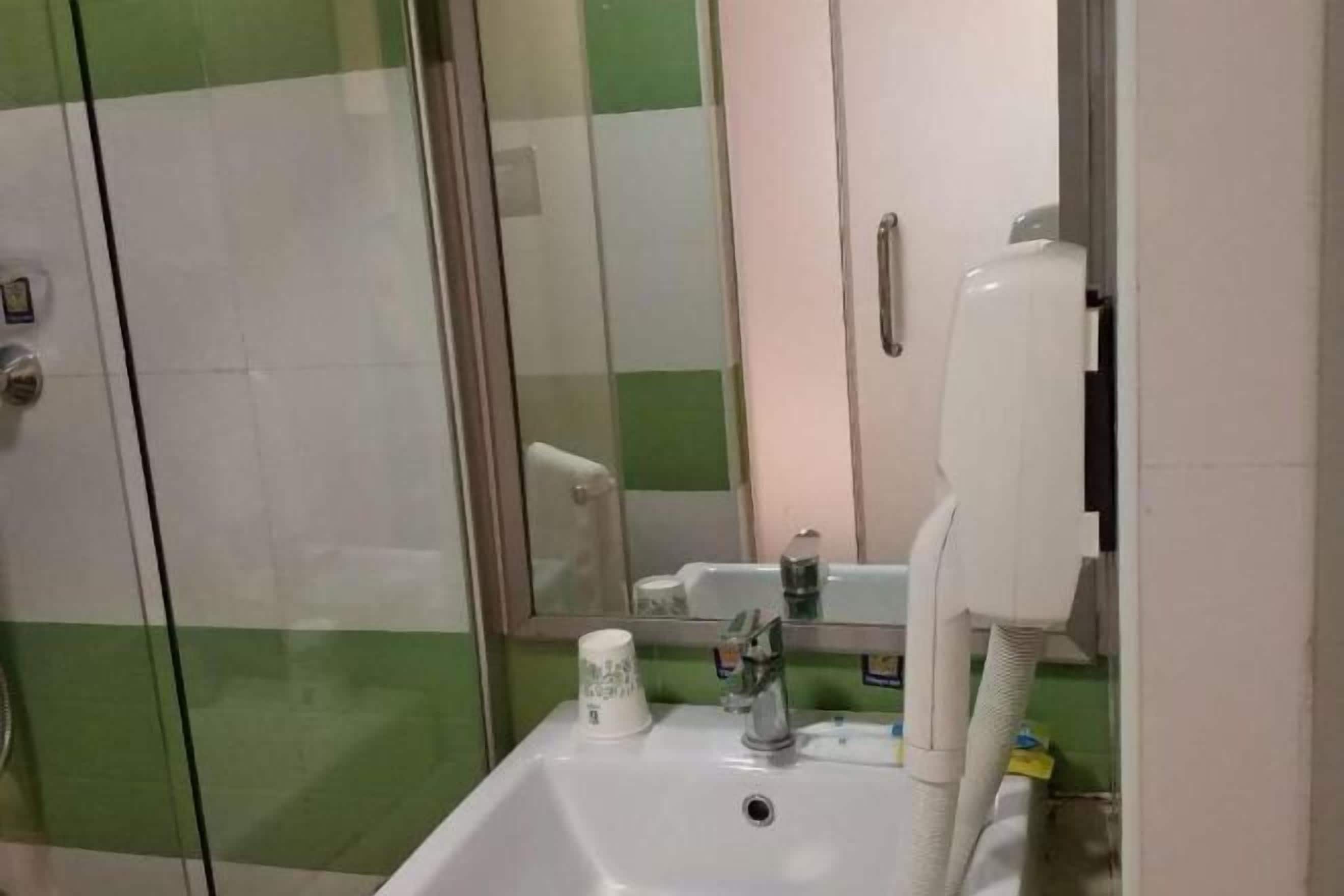 A bathroom with a sink, a mirror, a glass shower enclosure, and a hand dryer.