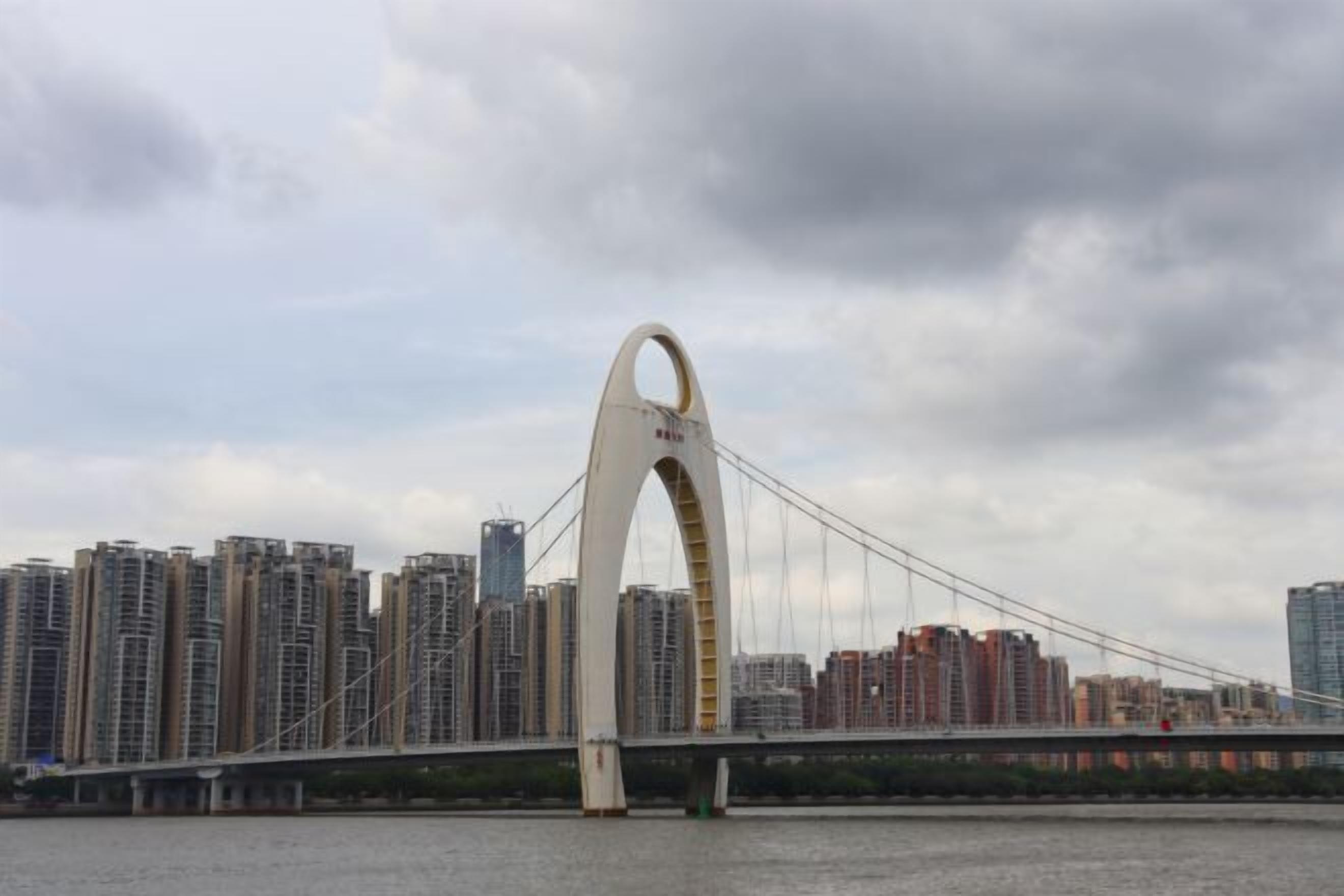 A large suspension bridge with a distinctive arch design, spanning over a body of water with high-rise buildings in the background.
