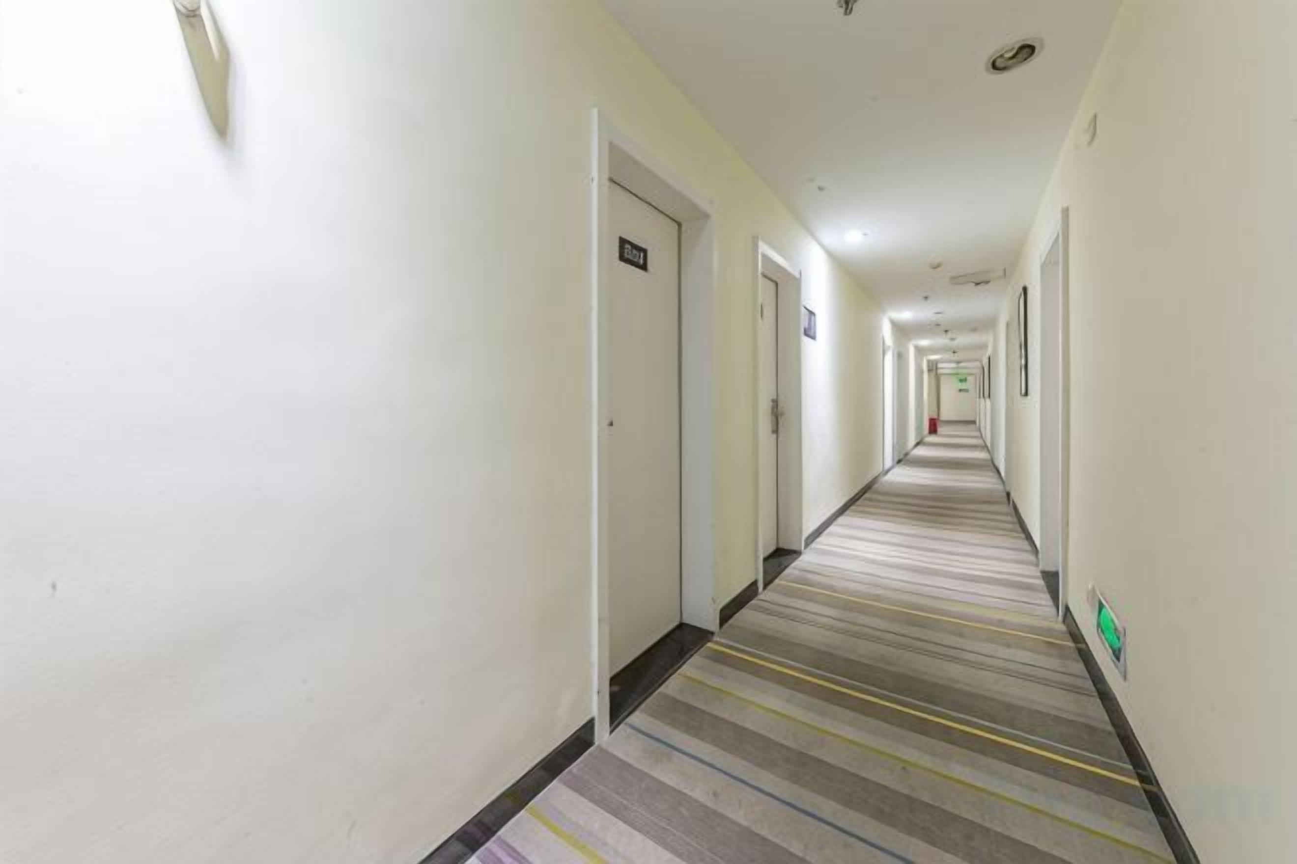 Pasillo de hotel con puertas a ambos lados, piso alfombrado y pared de color claro.