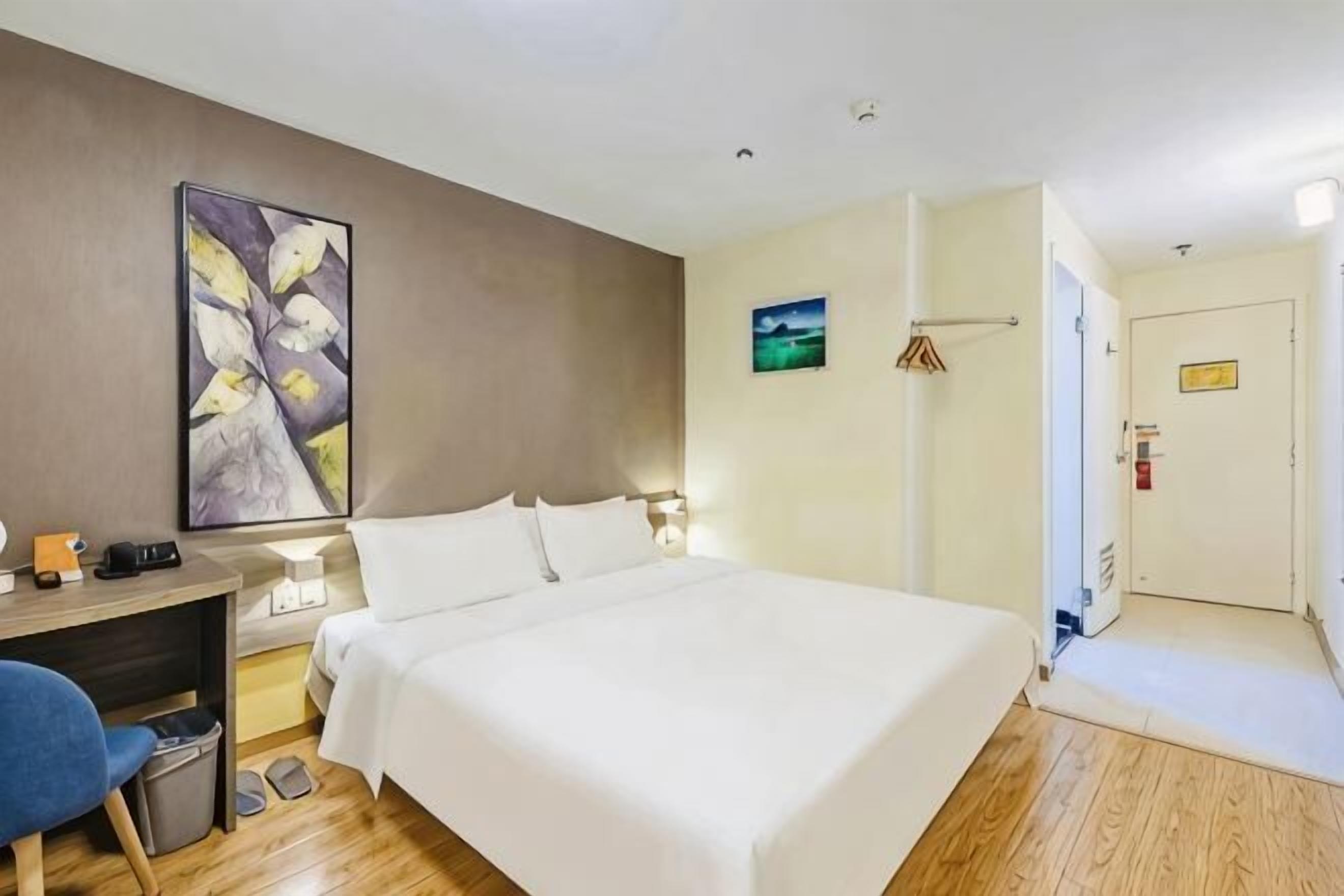 A hotel room with a bed, desk, chair, and artwork on the wall.