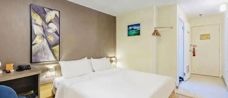 A hotel room with a bed, desk, chair, and artwork on the wall.