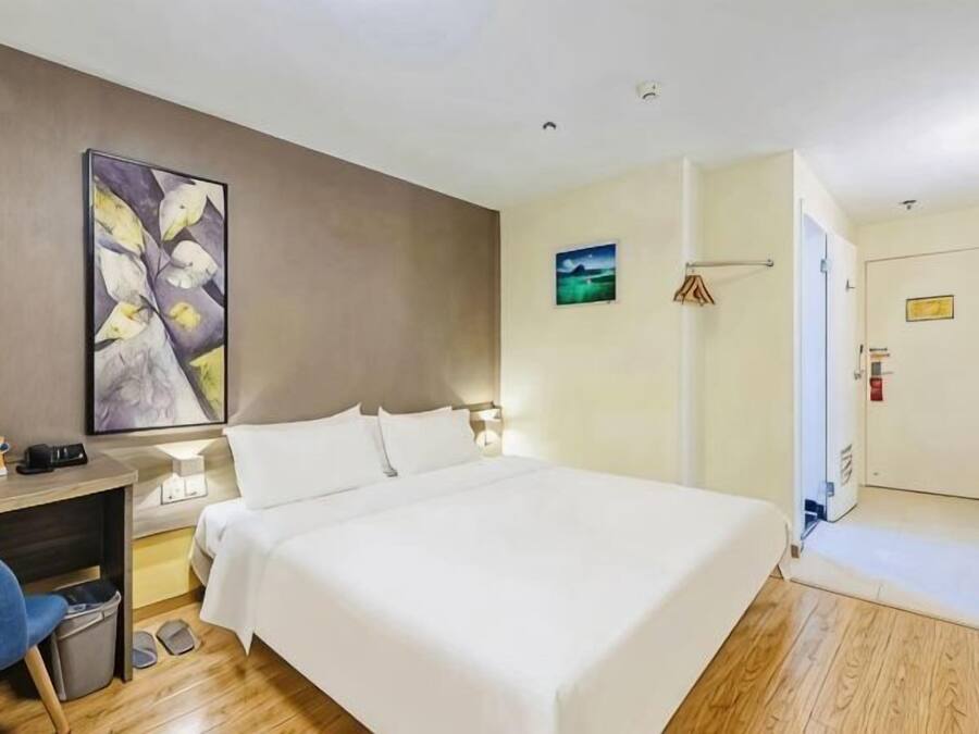 A hotel room with a bed, desk, chair, and artwork on the wall.