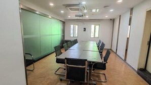 Un salón de conferencias con una larga mesa, sillas, un proyector y una pared con pantalla verde.