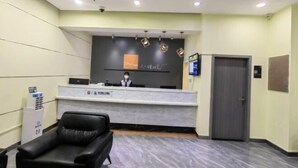 Un área de recepción con un escritorio, una silla para huésped, una pantalla en la pared y una puerta.