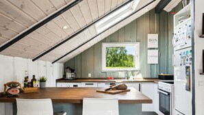 Et moderne køkken med en træø med barstole, et vindue med udsigt til grønne omgivelser, og et skilt der siger "BON COFFEE".