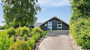 Et hus med en belagt indkørsel, der fører til en mørkeblå bygning, omgivet af velplejede haver og hække.