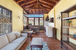 A cozy living area with a sofa, dining table, and kitchen area with a tiled floor and wooden ceiling.