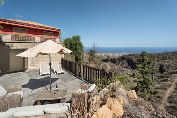 A terrace with wicker furniture, a table with a bottle and glass, and a view of the sea.
