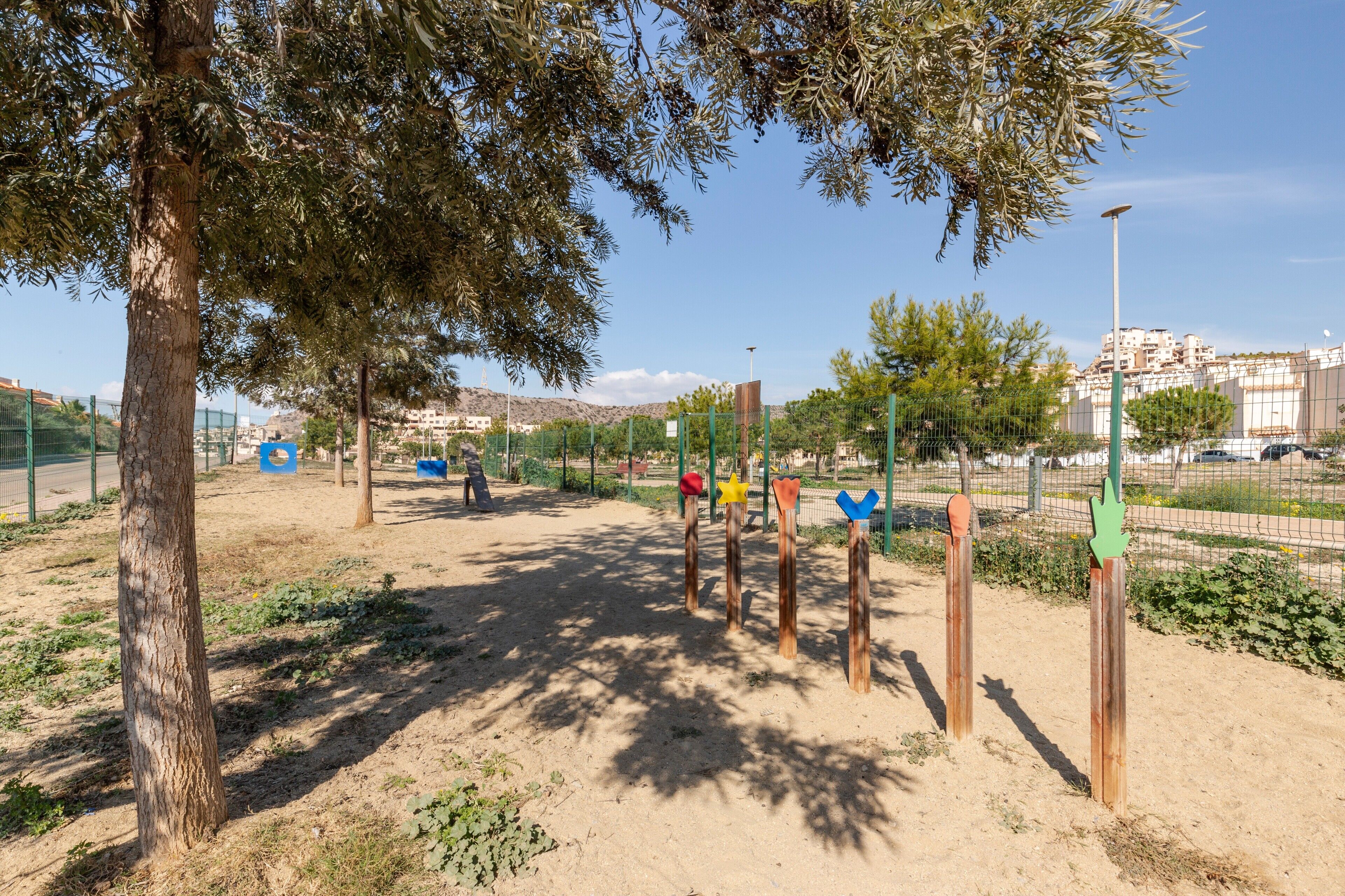 Un terrain de jeux avec du sable, des arbres et une clôture.