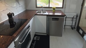 Una cocina compacta con estufa integrada, un lavabo y una ventana con vistas a edificios y árboles.