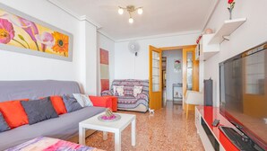 Una sala de estar con un sofá, una mesa de centro, un televisor y una puerta que da a otra habitación.