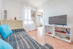 Un salon avec un canapé, un téléviseur, une étagère remplie de jouets et une porte donnant sur l’extérieur.