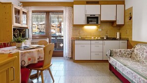 A compact kitchen with a dining area, wooden cabinets, a microwave, and a sofa. - Apartment 'Appartamento 2-3 Persone' with Mountain View, Balcony and Wi-Fi (Canazei)