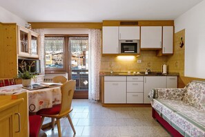 Cocina compacta con comedor, armarios de madera, microondas y sofá.