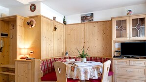 A cozy room with a wooden bench, a table with a white tablecloth, a television, and wooden cabinets. - Apartment 'Appartamento 2-3 Persone' with Mountain View, Balcony and Wi-Fi (Canazei)