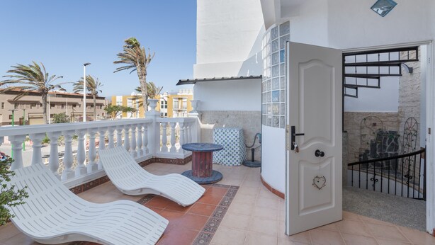 Een balkon met witte lounge fauteuils, een klein rond tafeltje en een deur naar een trap.