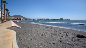 Een strand met een kiezelstrand, heldere lucht en een berg in de verte.